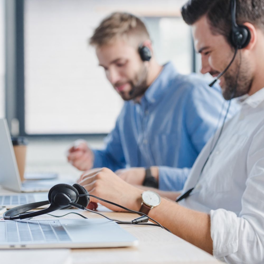 smiling-young-call-center-operators-in-headsets-using-laptops-in-office.jpg